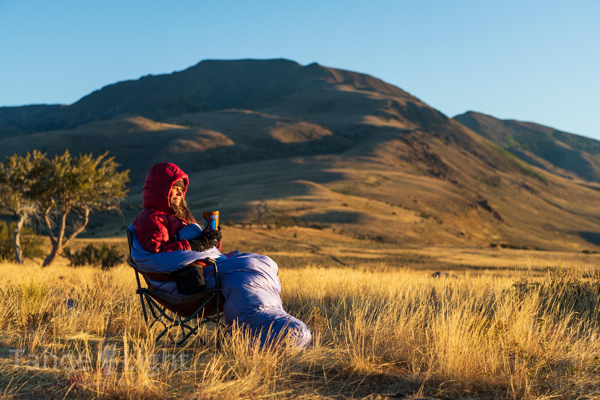 photograph of woman having morning coffe in sleeping bag